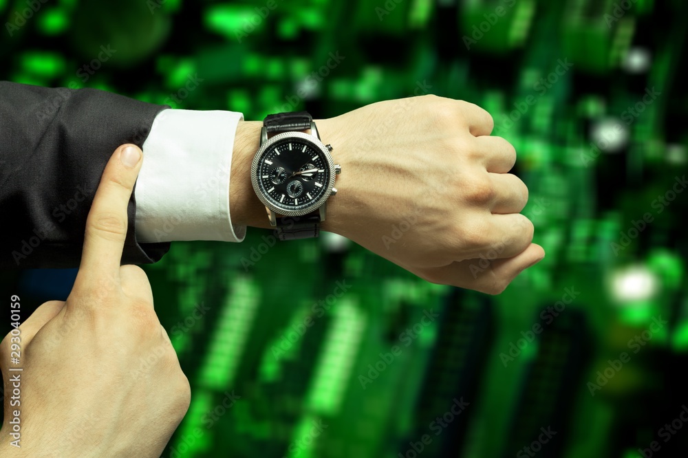 Businessman pointing at hand watch on grey wall background, close-up