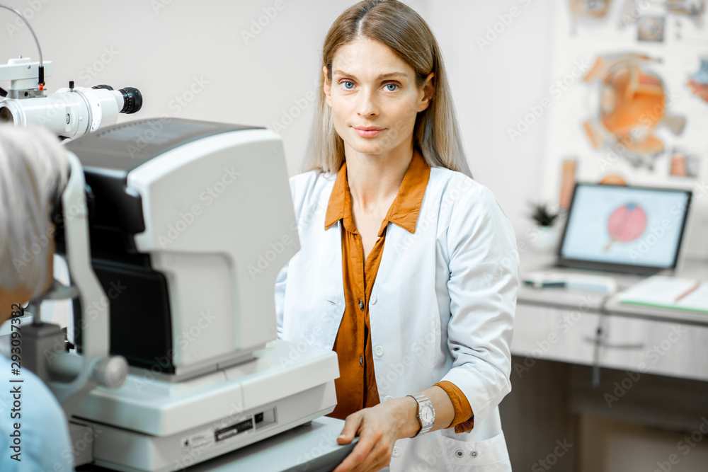 Portrait of a female ophthalmologist examining eyes of a senior patient using digital microscope dur