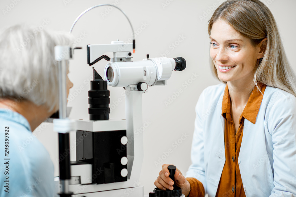 Cheerful ophthalmologist examining eyes of a senior patient using microscope during a medical examin