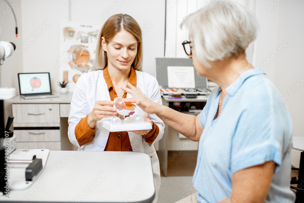 Female ophthalmologist showing the eye model to a senior patient during a medical consultation in th