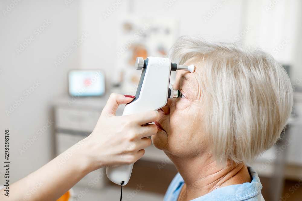 Doctor measuring the eye pressure with modern tonometer to a senior patient in the medical office, c