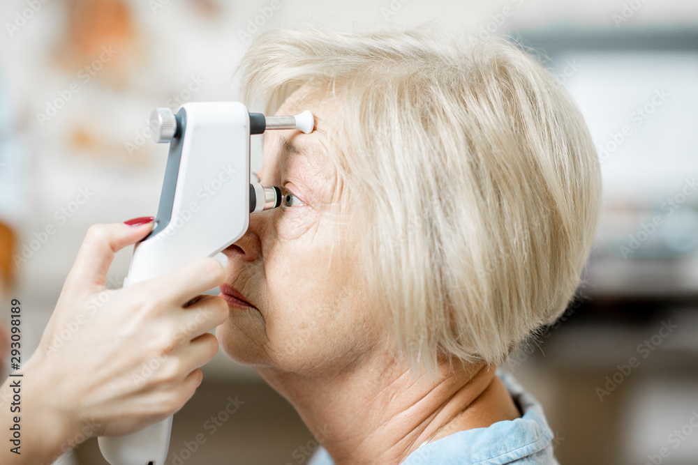 Doctor measuring the eye pressure with modern tonometer to a senior patient in the medical office, c