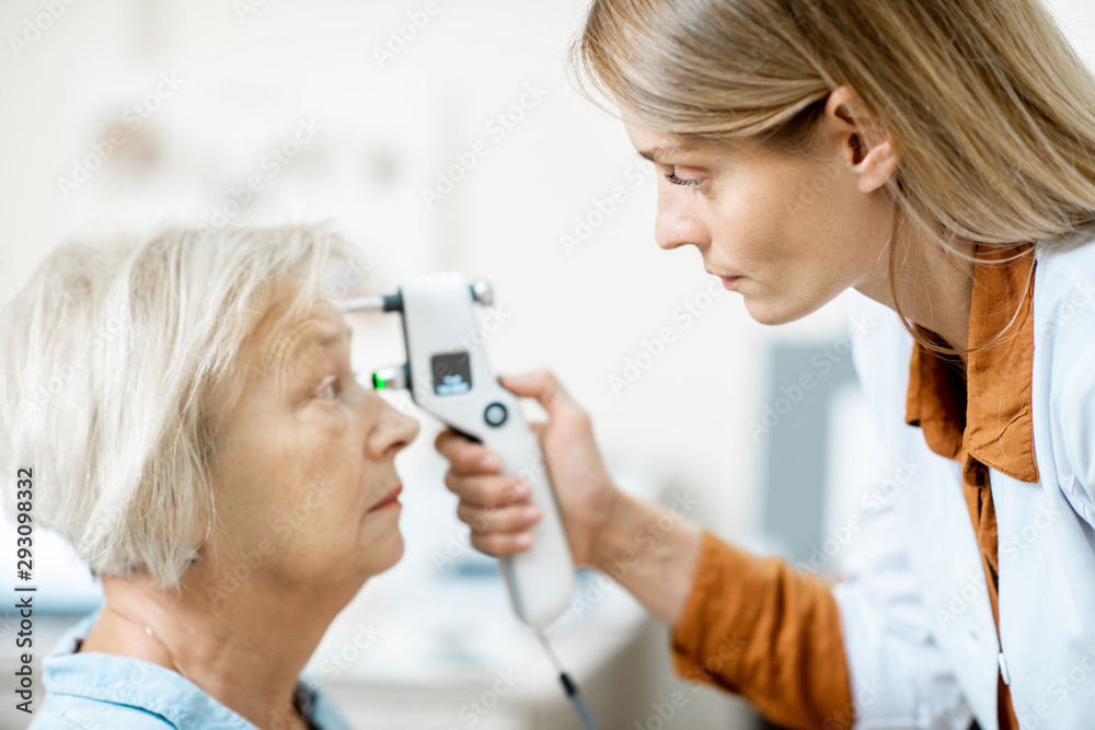 Female ophthalmologist measuring the eye pressure with modern tonometer to a senior patient in the m