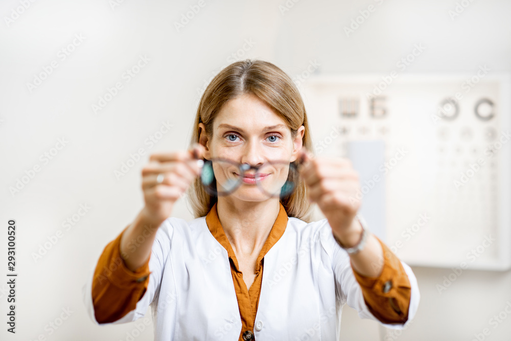 Ophthalmologist offering eyeglasses putting them forward to the camera, standing in front of eye cha