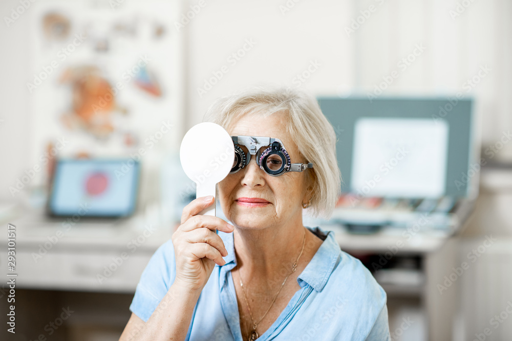 Senior woman checking vision with eye test glasses and scapula during a medical examination at the o