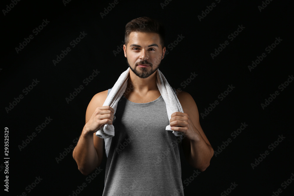 Sporty young man with towel on dark background