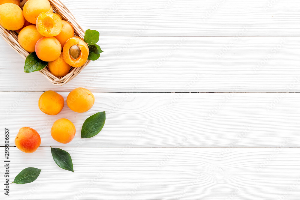 Fresh raw apricots in basket on white wooden background top view copy space, pattern with leaves