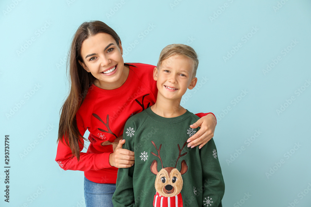 Little boy and his mother in Christmas sweaters on color background