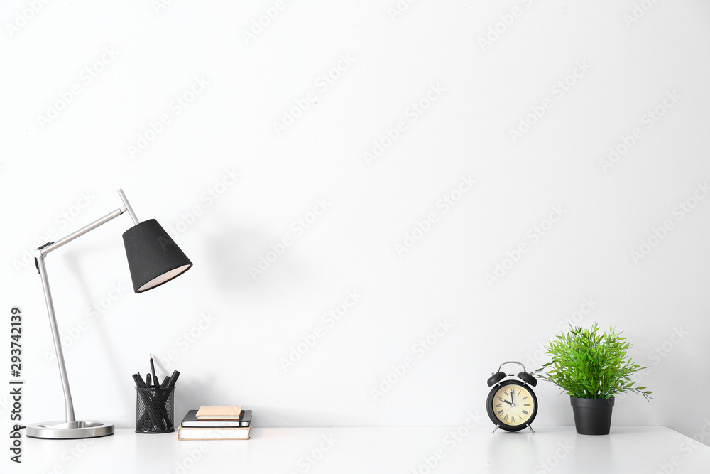 Modern workplace with alarm clock, lamp and stationery near white wall