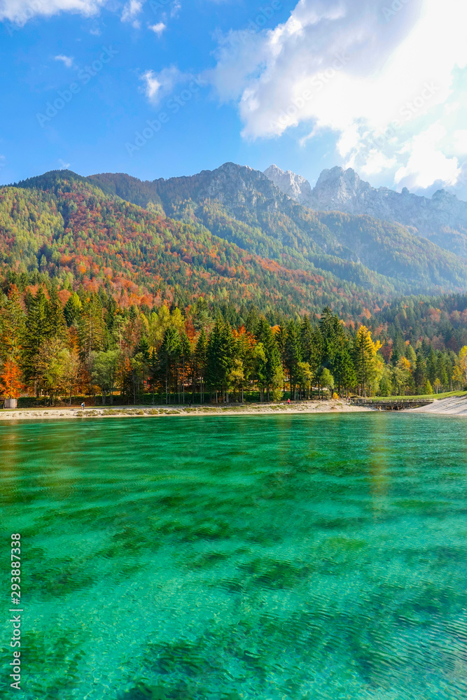 Spectacular shot of colorful forest covered mountain towering over emerald lake.