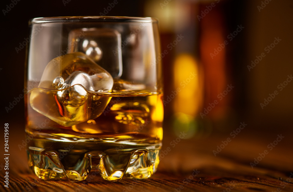 Whiskey with ice cubes. Glass of Whisky and the bottle on wooden table over dark background. Glass o