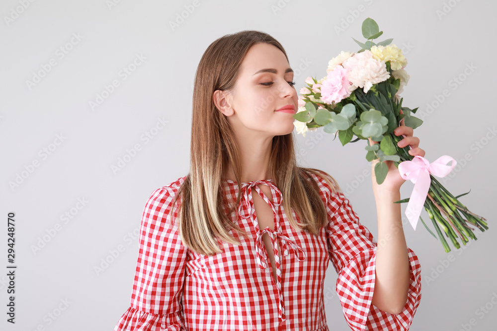 Beautiful young woman with bouquet of carnation flowers on light background