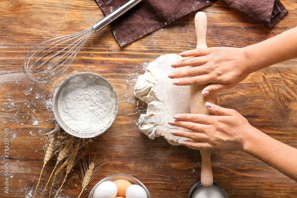 Woman rolling out dough on wooden background