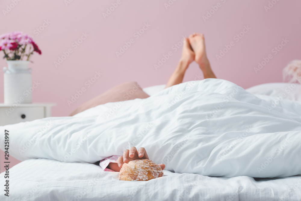 Young woman reaching hand for tasty bun while lying in bed