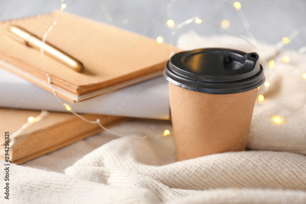 Cup of coffee with notebooks and garland on table, closeup