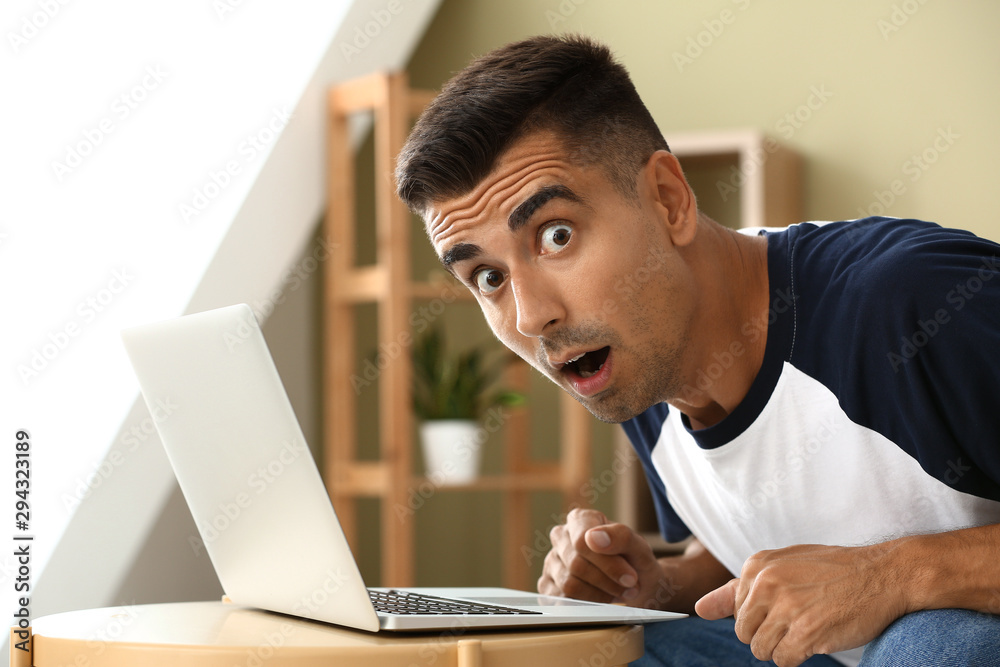 Shocked young man with laptop at home