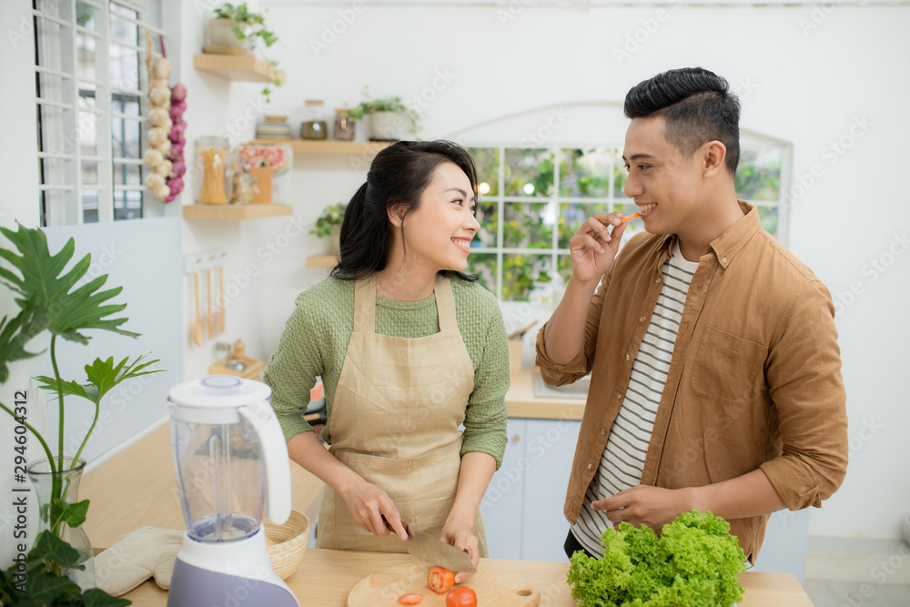 一对美丽的年轻亚洲夫妇在家里的厨房里烹饪健康食品时，谈笑风生