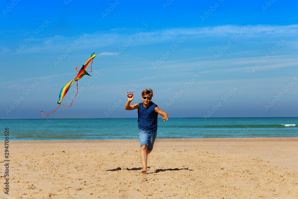 Handsome boy in blue shirt run with kite near sea