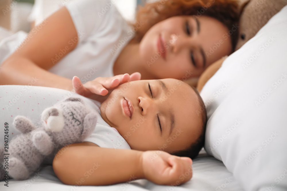 Young African-American woman and her sleeping baby on bed