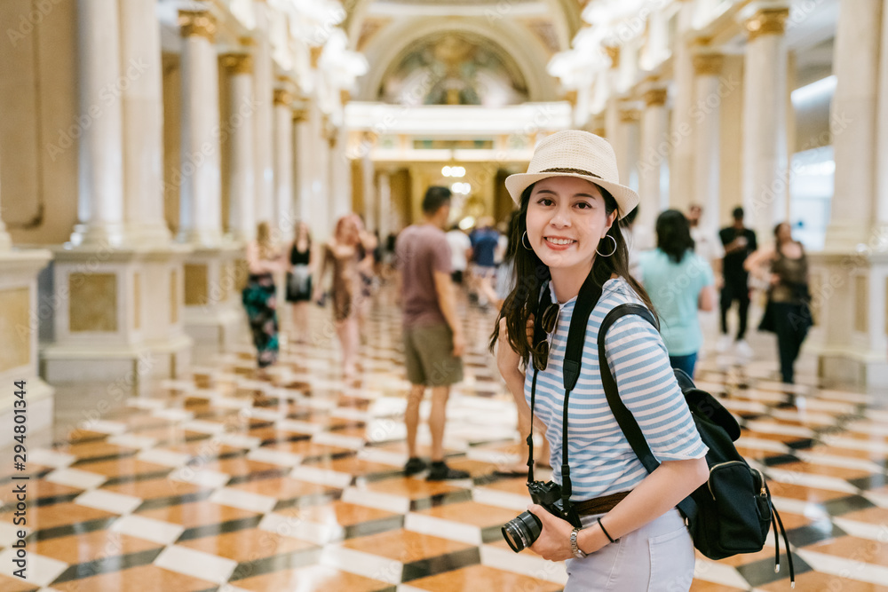 joyful female tourist walk inside Palace in romania. charming girl travel backpacker face camera smi