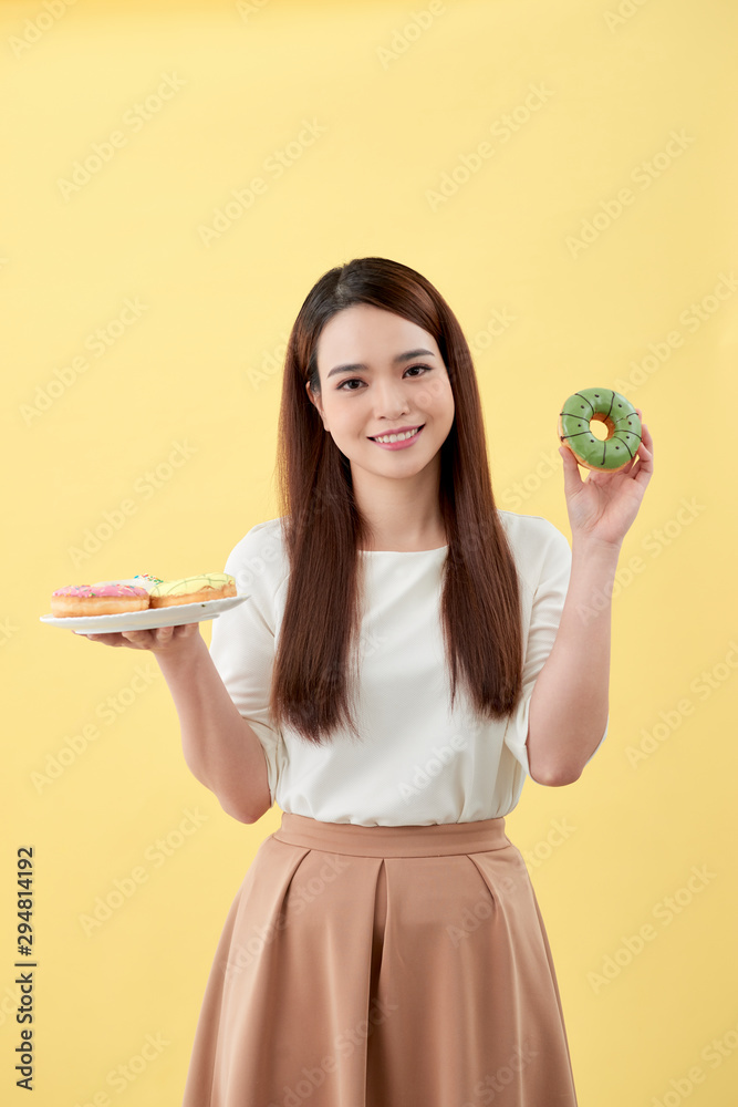 有魅力的女孩拿着新鲜的甜甜圈，用甜食玩得很开心。心情好，饮食理念好。