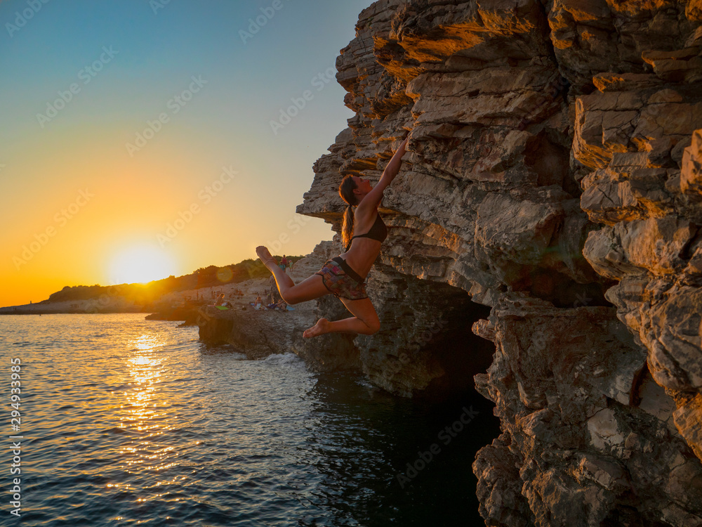 阳光灿烂：在一个阳光明媚的夏夜，一个强壮的女孩爬上了一个充满挑战的悬崖。