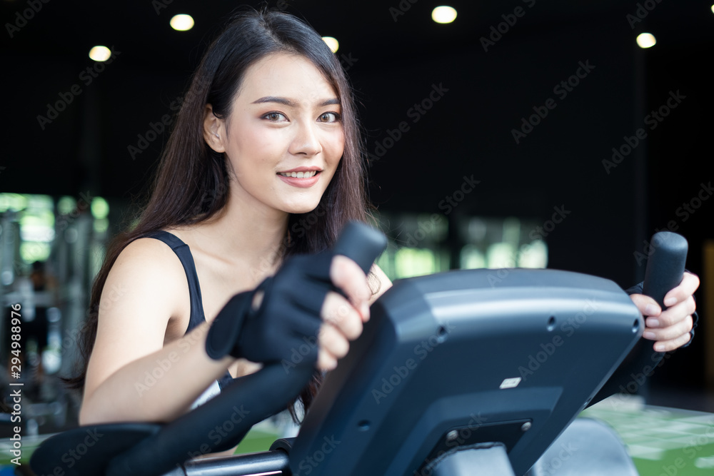 Crop shot of Asian beautiful sporty young woman workouts in Gym or fitness club. The girl cycling on