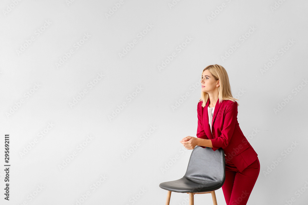 Beautiful stylish businesswoman with chair on light background