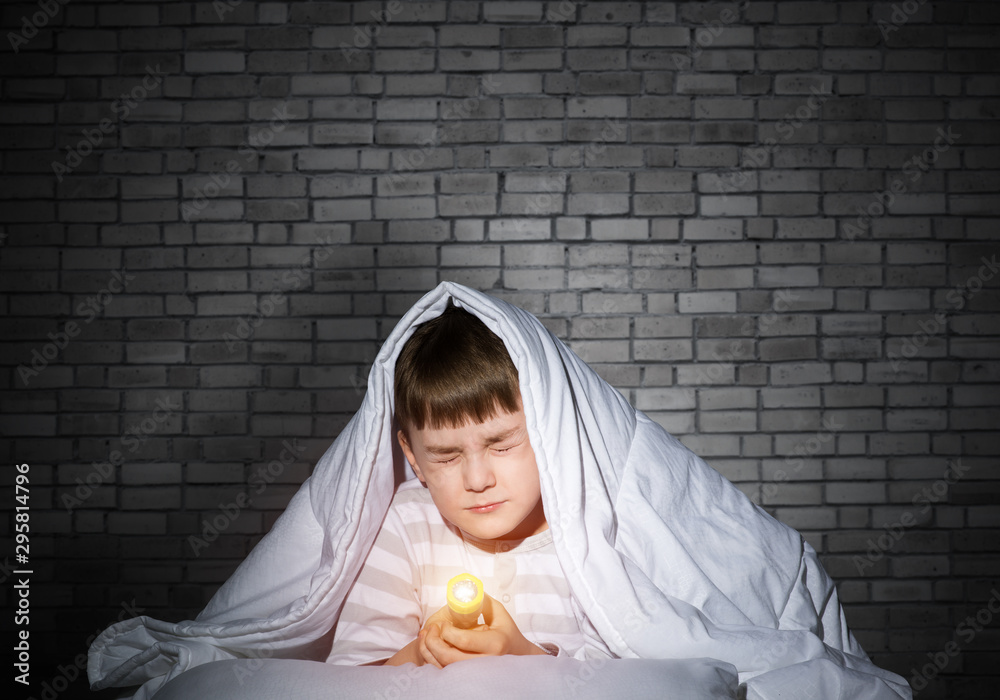 Frightened child with flashlight under blanket