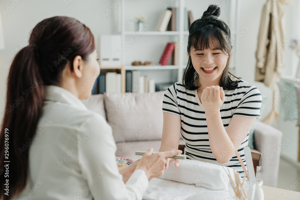 漂亮的年轻女孩客户在招待所和美甲师一起大笑，玩得很开心。亚洲快乐j