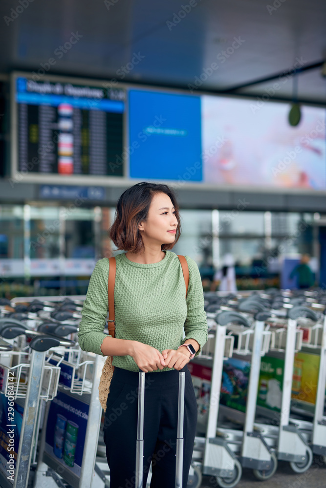 Asian young woman standing with suitcase while waiting her bus in the airport.