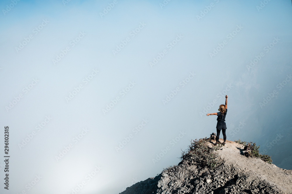 戴着防护口罩的年轻女子在火山口酸湖上方的活火山Kawah Ijen山顶与po合影