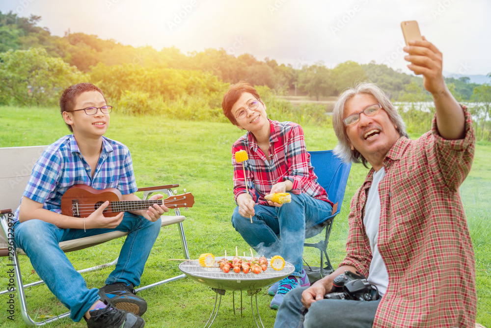 Asian Senior male taking photo his wife and son by smart phone while they’re on vacation camping.