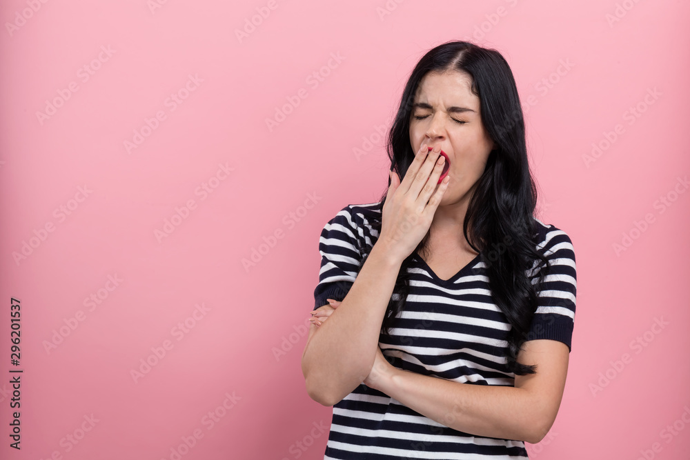 Young woman yawning on a pink background