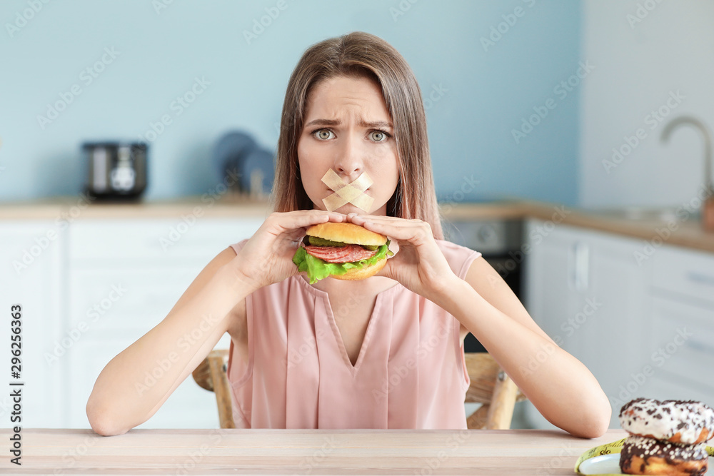 悲伤的女人，嘴巴被胶带封住，厨房里有美味的汉堡。饮食概念