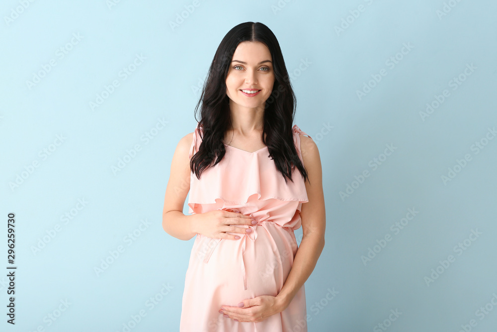 Beautiful young pregnant woman on color background