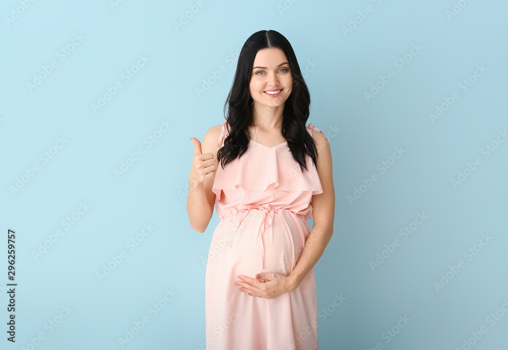 Beautiful young pregnant woman showing thumb-up on color background