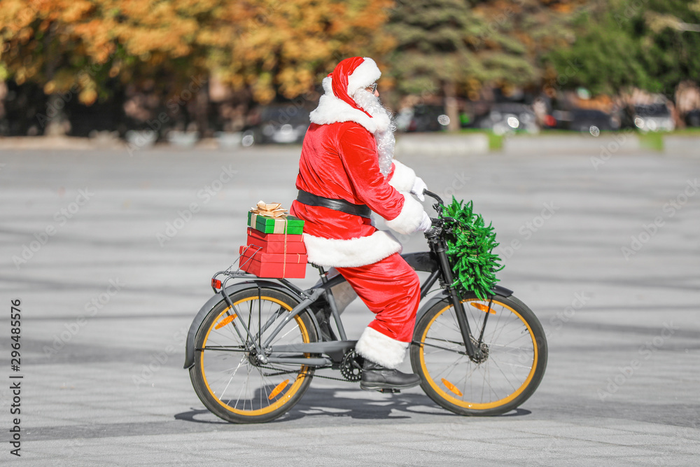 Santa Claus with Christmas gifts riding bicycle outdoors