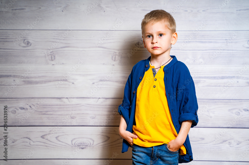 Portrait of a beautiful kid boy in yellow T-shirt and denim jacket, shirt. Boy standing on a white w