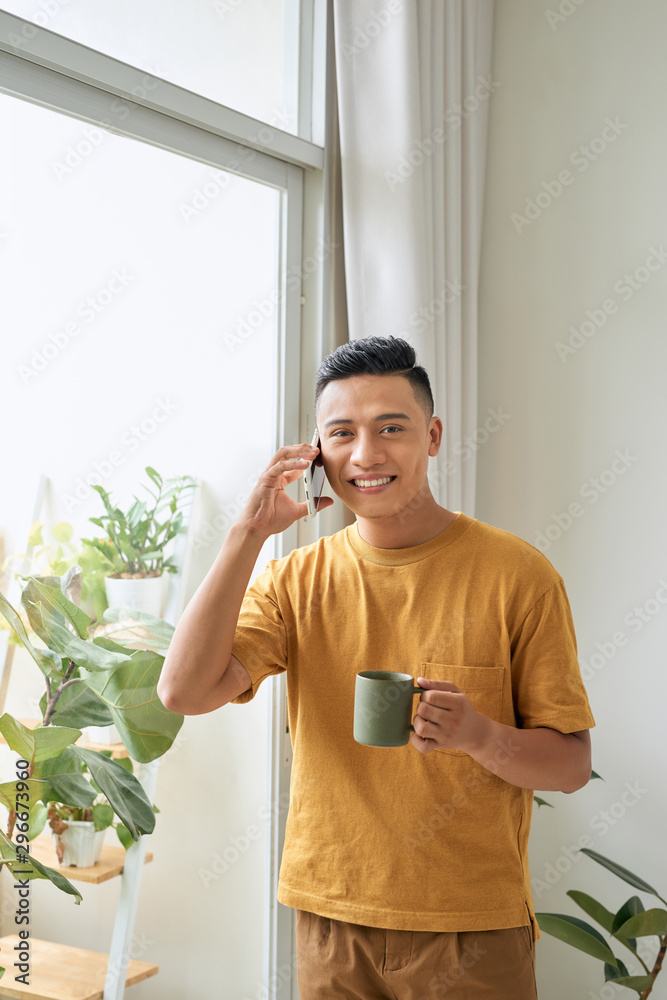 一个穿着休闲服的年轻人早上在窗户边打手机