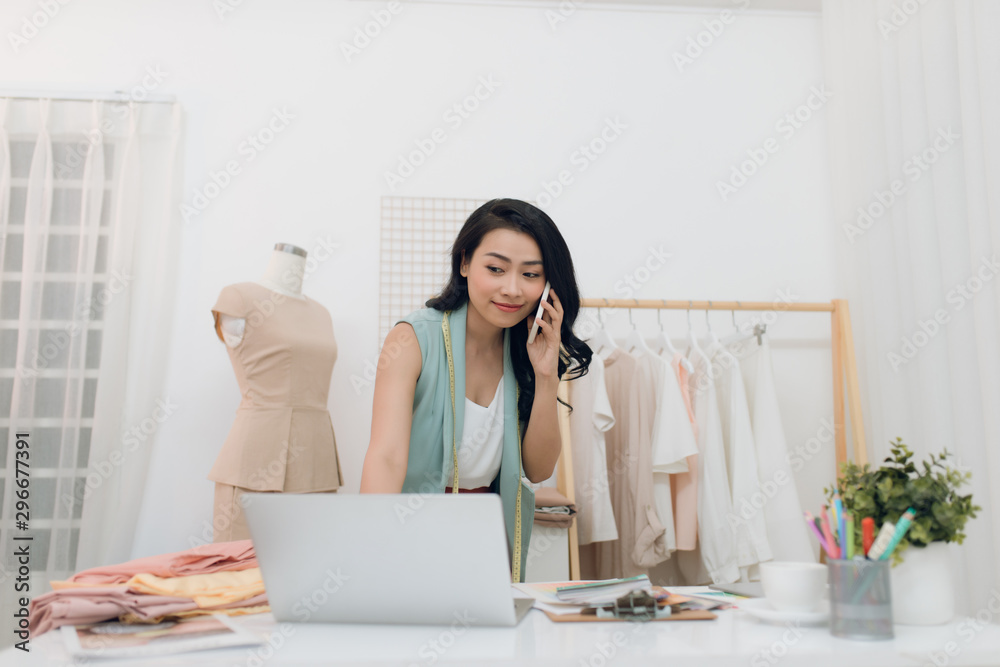 Young Asian fashion designer/business using laptop and calling at her studio