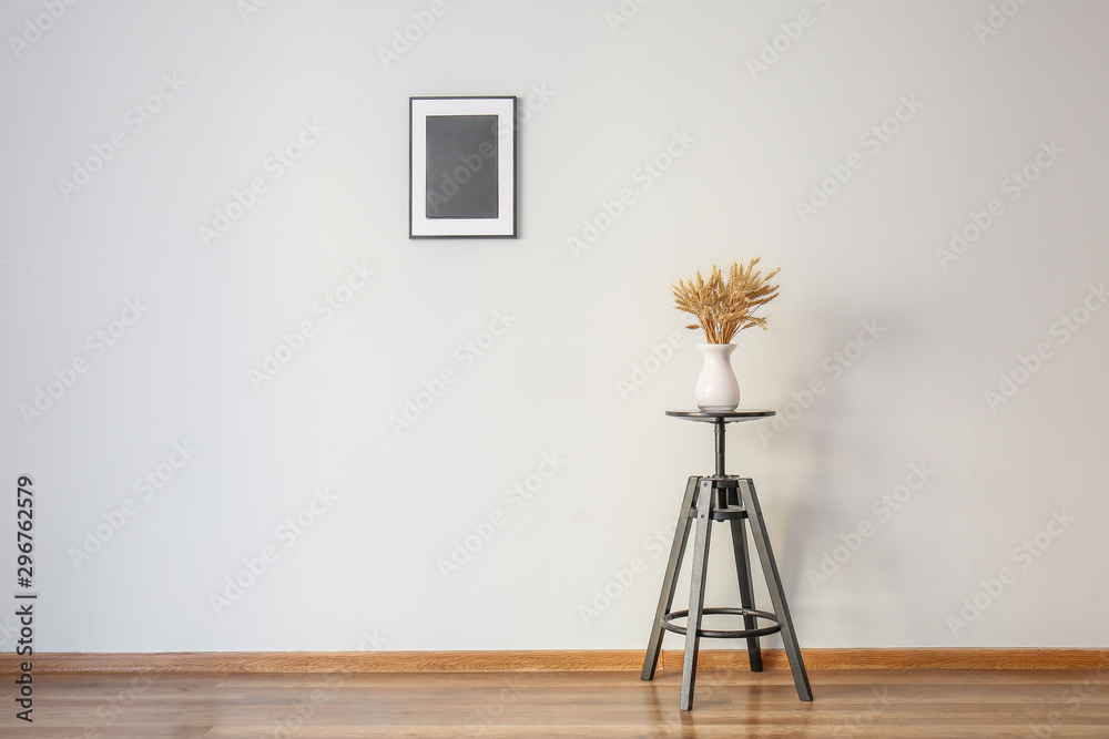 Table with wheat spikelets in vase and photo frame on white wall in room