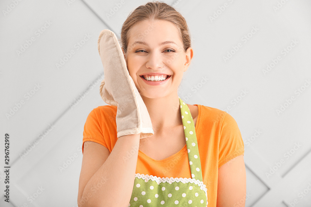 Beautiful young woman in apron on light background