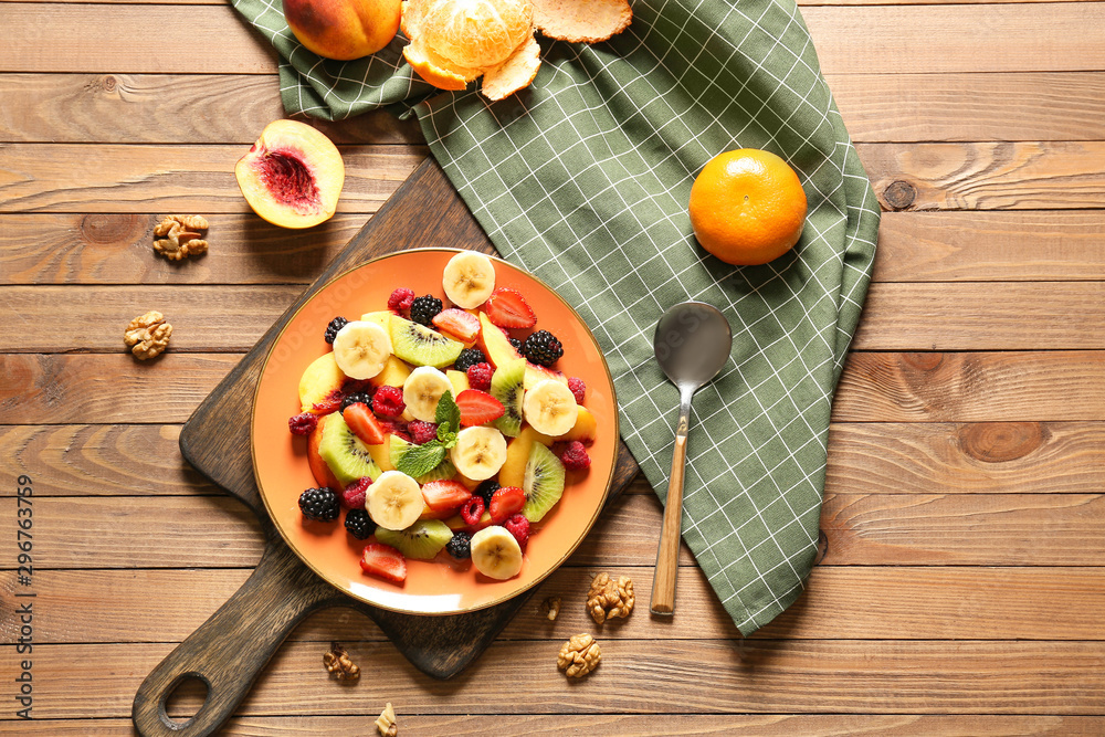 Plate with tasty fruit salad on wooden table