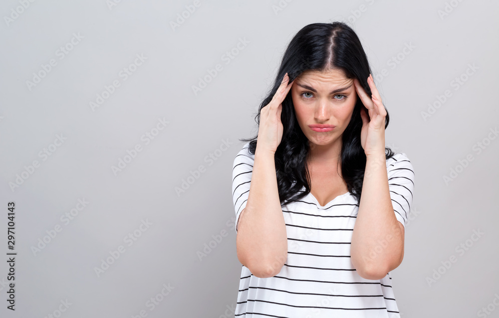 Young woman suffering from headache on a gray background