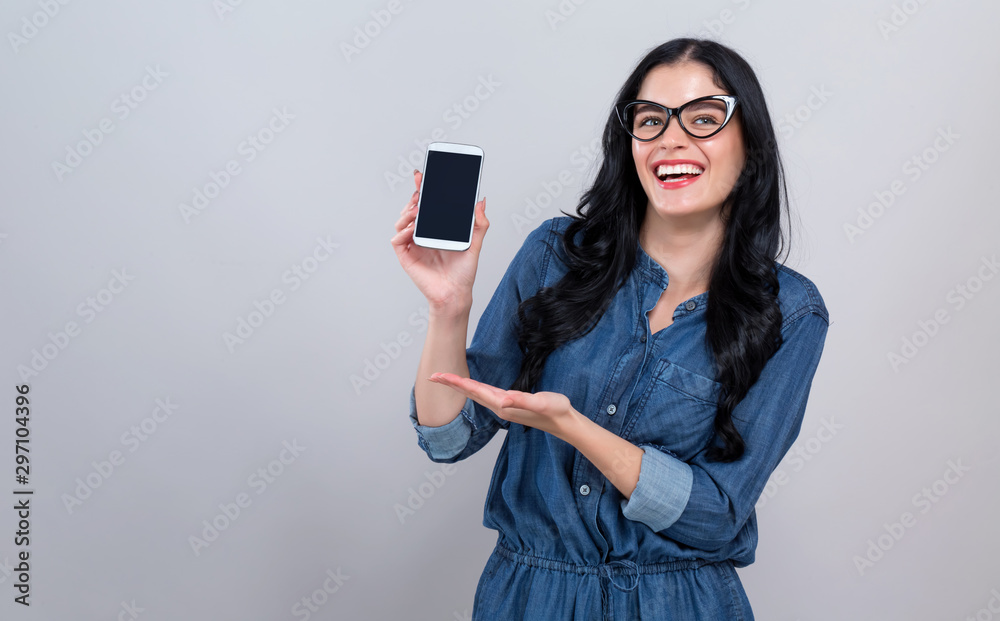 Young woman holding out a cellphone in her hand on a gray background