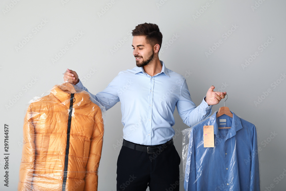 Male worker of modern dry-cleaner with clothes on light background