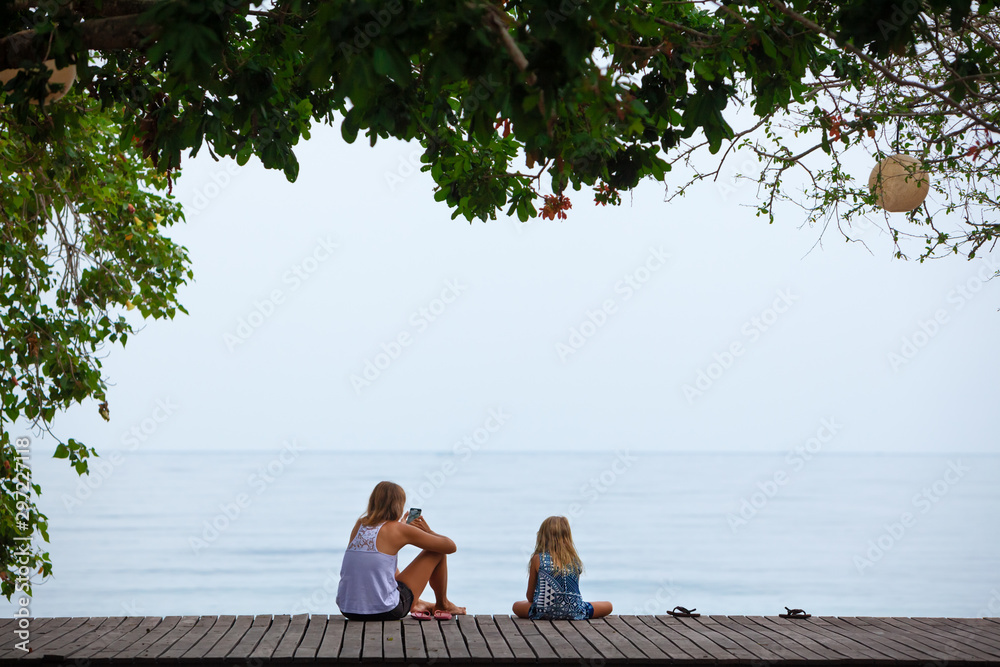 Happy mother, child relaxing and talking on luxury hotel veranda with beautiful view. People looking