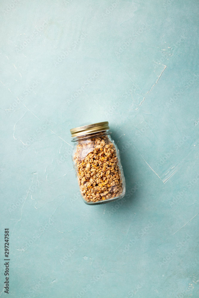 Home granola in a glass jar on blue concrete background