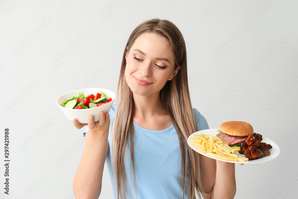 在浅色背景下吃健康和不健康食物的女性。饮食概念